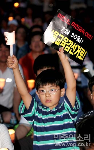 지난 5일 촛불문화제에 참석한 한 어린이가 '미친소, 미친교육 OUT 7월30일 서울교육감선거로!'라고 적힌 피켓을 들어 보이고 있다.